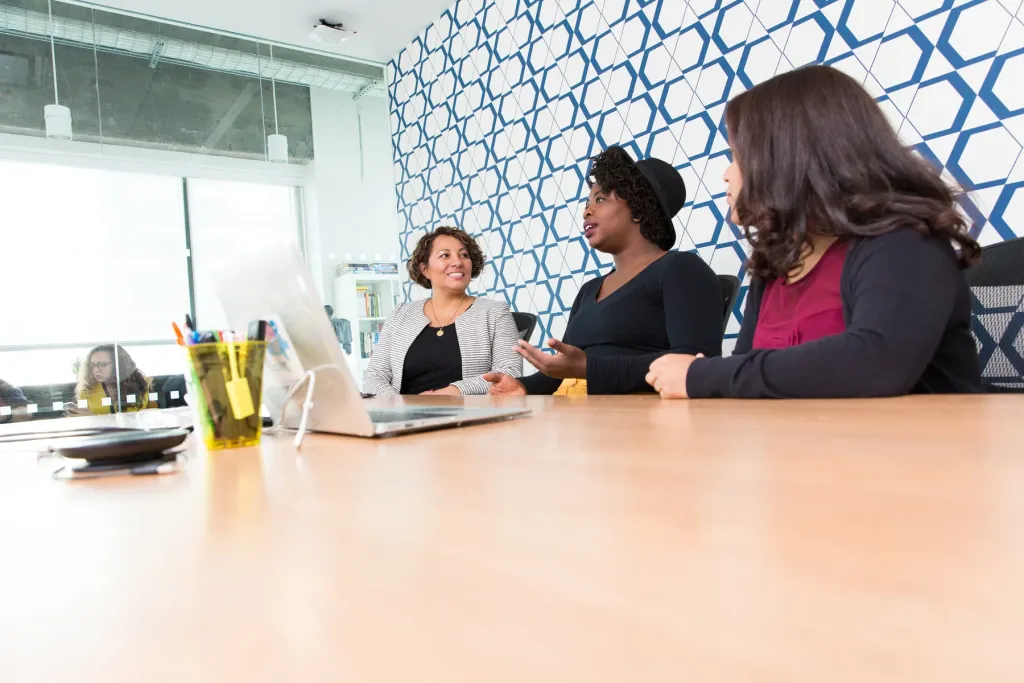 Photo: Mike Ngo / #WOCinTech Chat. Creative Commons Attribution. Stock photography. Three colleagues discussing their work around a table with an open laptop
